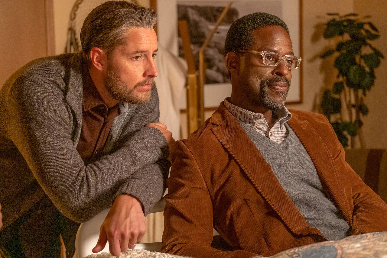 Justin Hartley and Sterling K. Brown, dressed in casual jackets and shirts, lean on a surface and look contemplative in an indoor setting