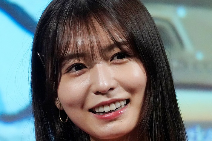 笑顔の女性。赤い服を着ており、前髪があり、肩にかかる長さの髪型。