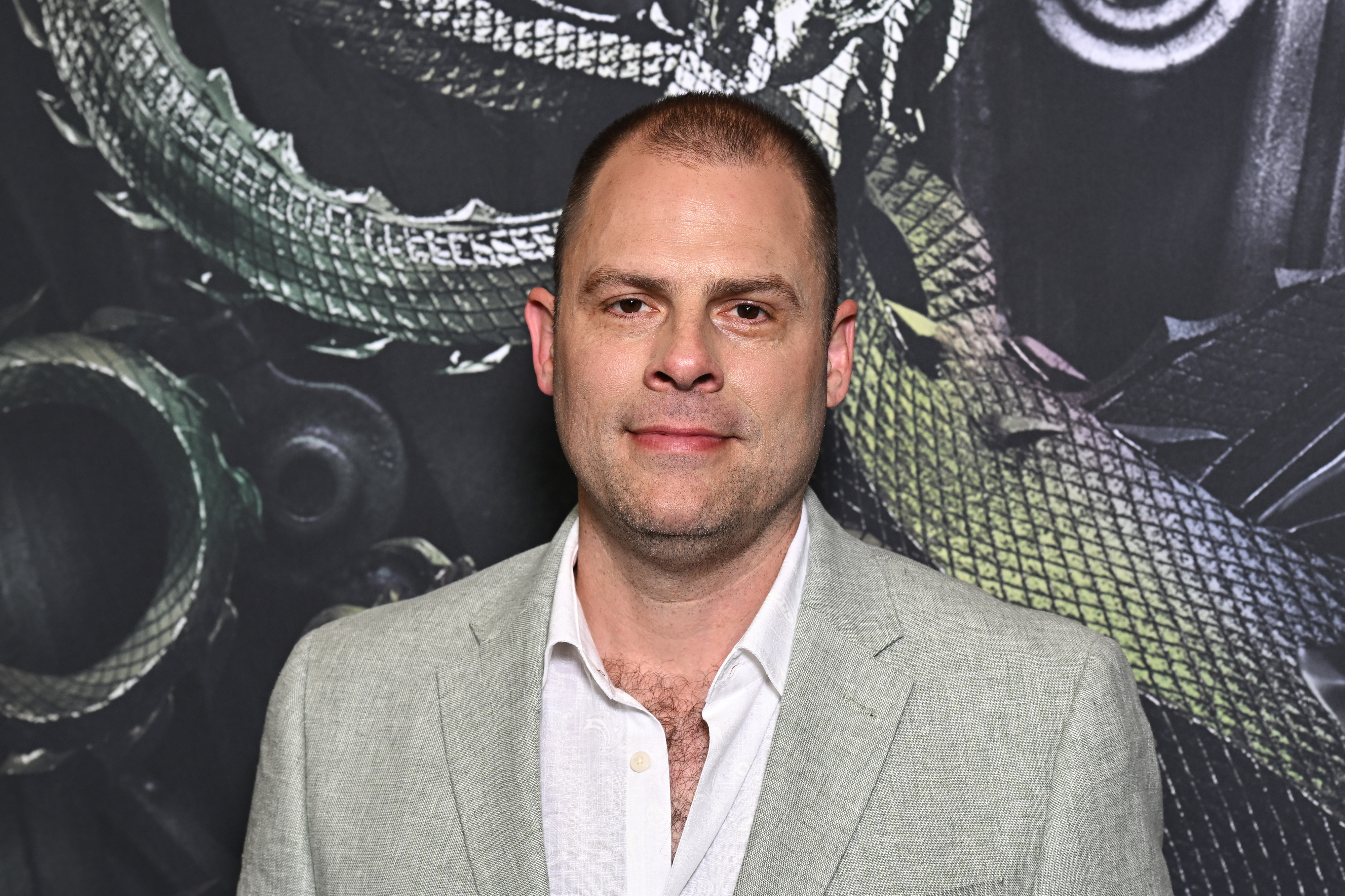 Ryan Condal in a light-colored suit and shirt poses in front of a backdrop featuring a dragon design