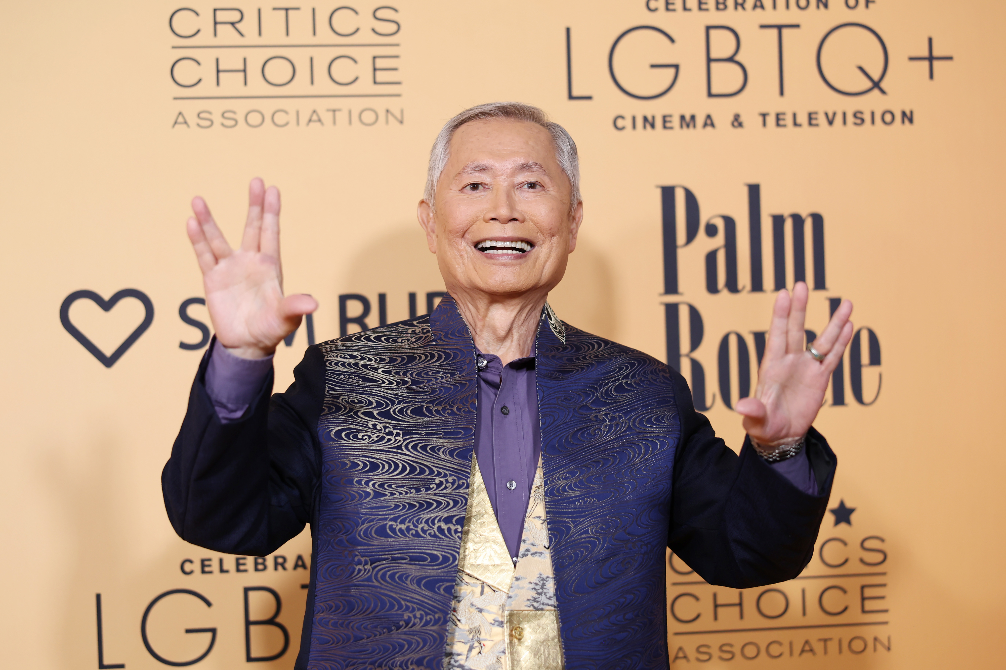 George Takei on the red carpet at the Critics Choice Association Celebration of LGBTQ+ Cinema &amp;amp; Television event, wearing a patterned jacket and smiling