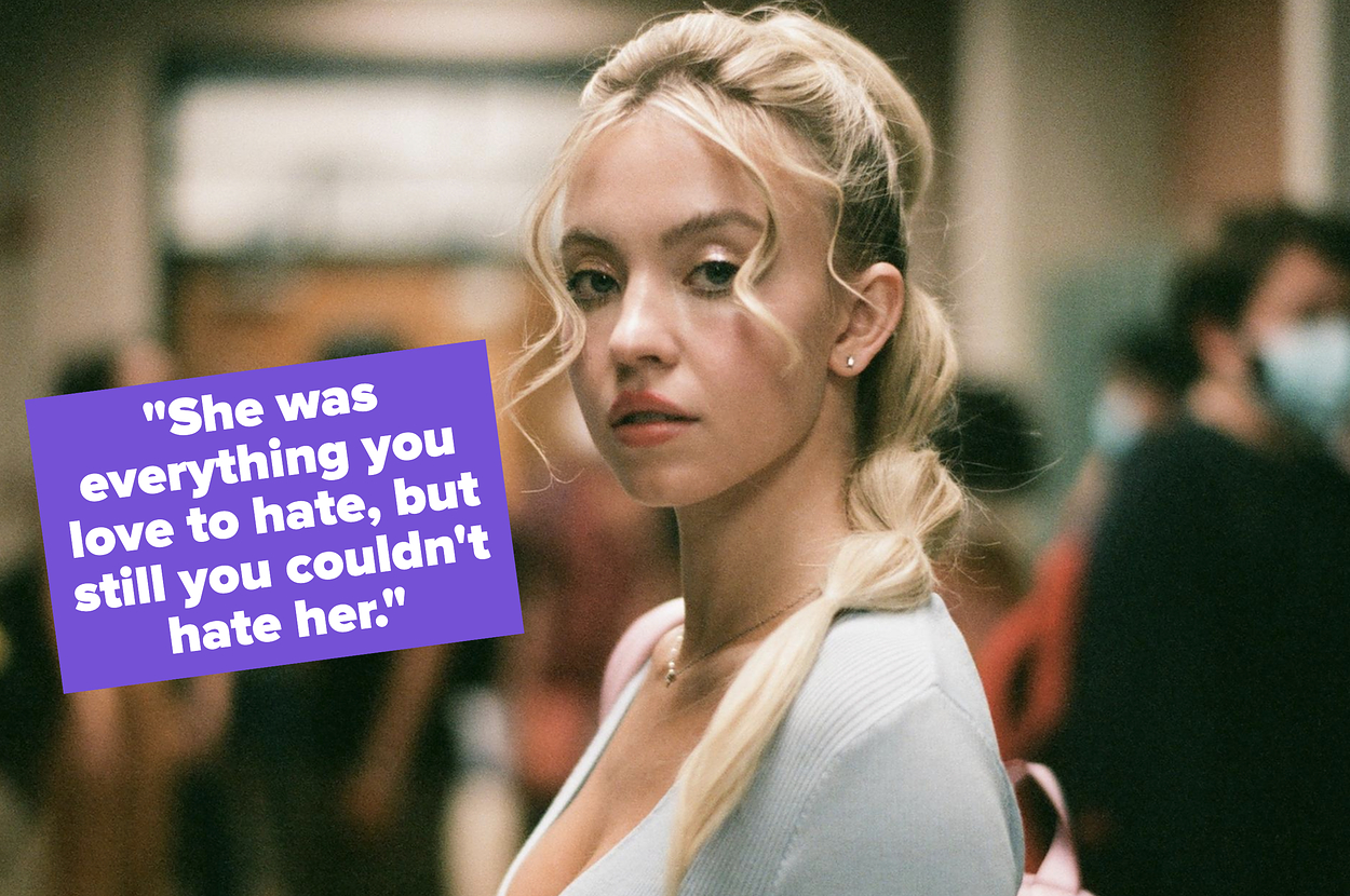 Sydney Sweeney wears a white top with her blonde hair styled in a ponytail, standing in a crowded indoor space, looking over her shoulder at the camera