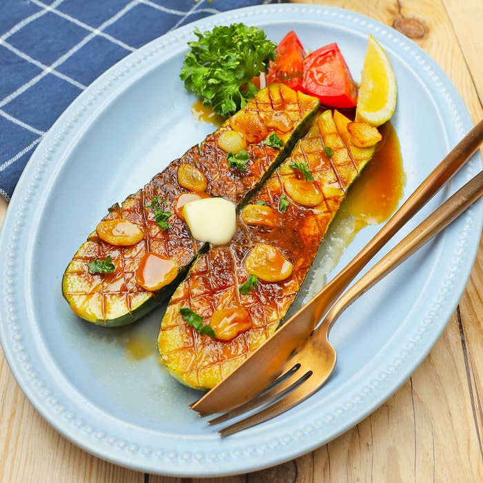 白いプレートに盛られたグリルされた野菜、ニンニクソースがかかり、レモンとパセリで飾られている。