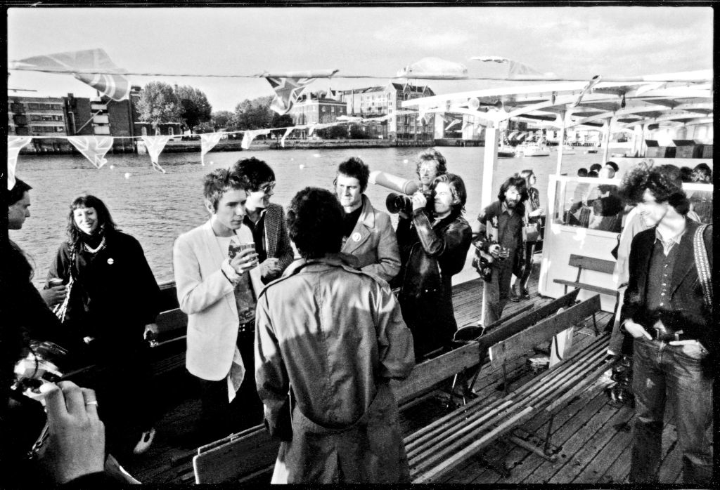 Newspaper reporters and photographers interview members of the Sex Pistols aboard a boat on the River Thames. Members include Johnny Rotten, Sid Vicious