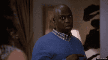A man in a blue sweater makes a funny and skeptical face while pointing at something off-screen