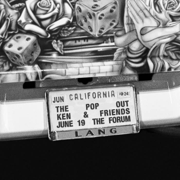 A license plate holder features a poster promoting a music event: &quot;The Pop Out,&quot; with Ken &amp; Friends performing on June 19 at The Forum in California