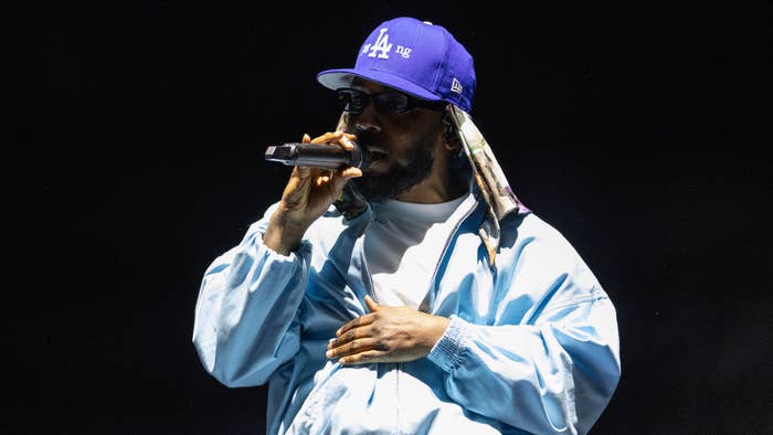 Kendrick Lamar on stage performing in a casual outfit with a blue jacket and LA cap