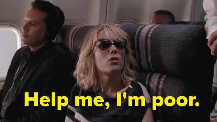 Kristen Wiig in black-and-white dress and sunglasses, sitting between two men on a plane