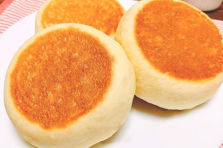 白い皿の上に3つの焼きたてのパンケーキが並んでおり、背景には赤いジャムの入った小皿が見える。