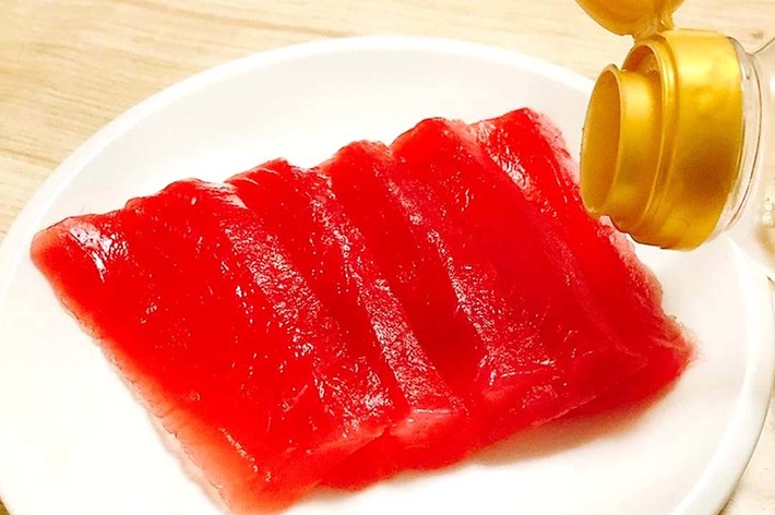 白い皿に盛られた4切れの赤身のまぐろの刺身に醤油がかけられている様子。