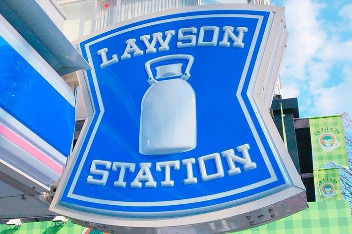 ローソンの看板が建物の外壁に設置されている。背景は都市の風景。