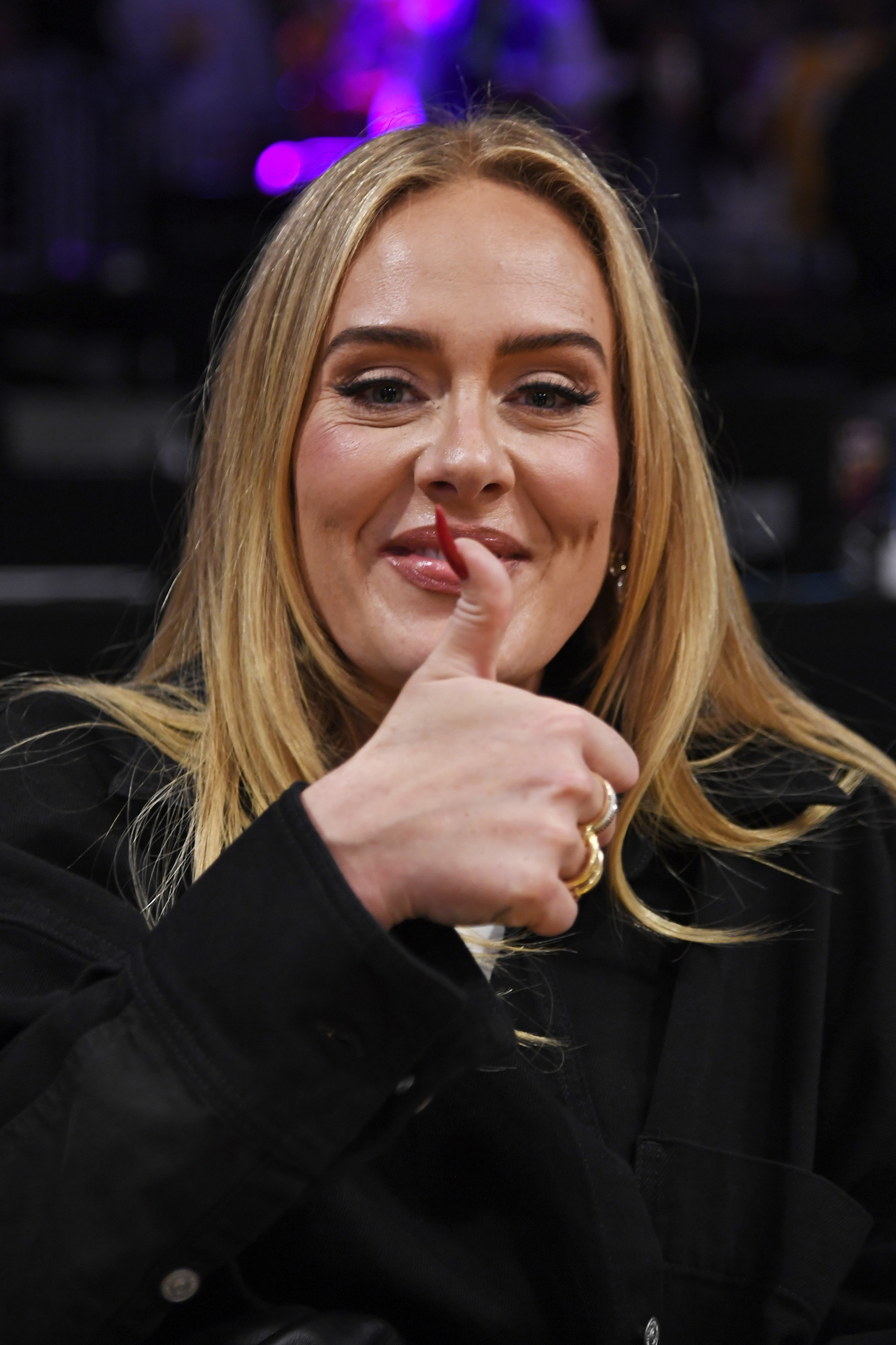 Adele gives a thumbs-up while smiling, dressed in a casual black shirt