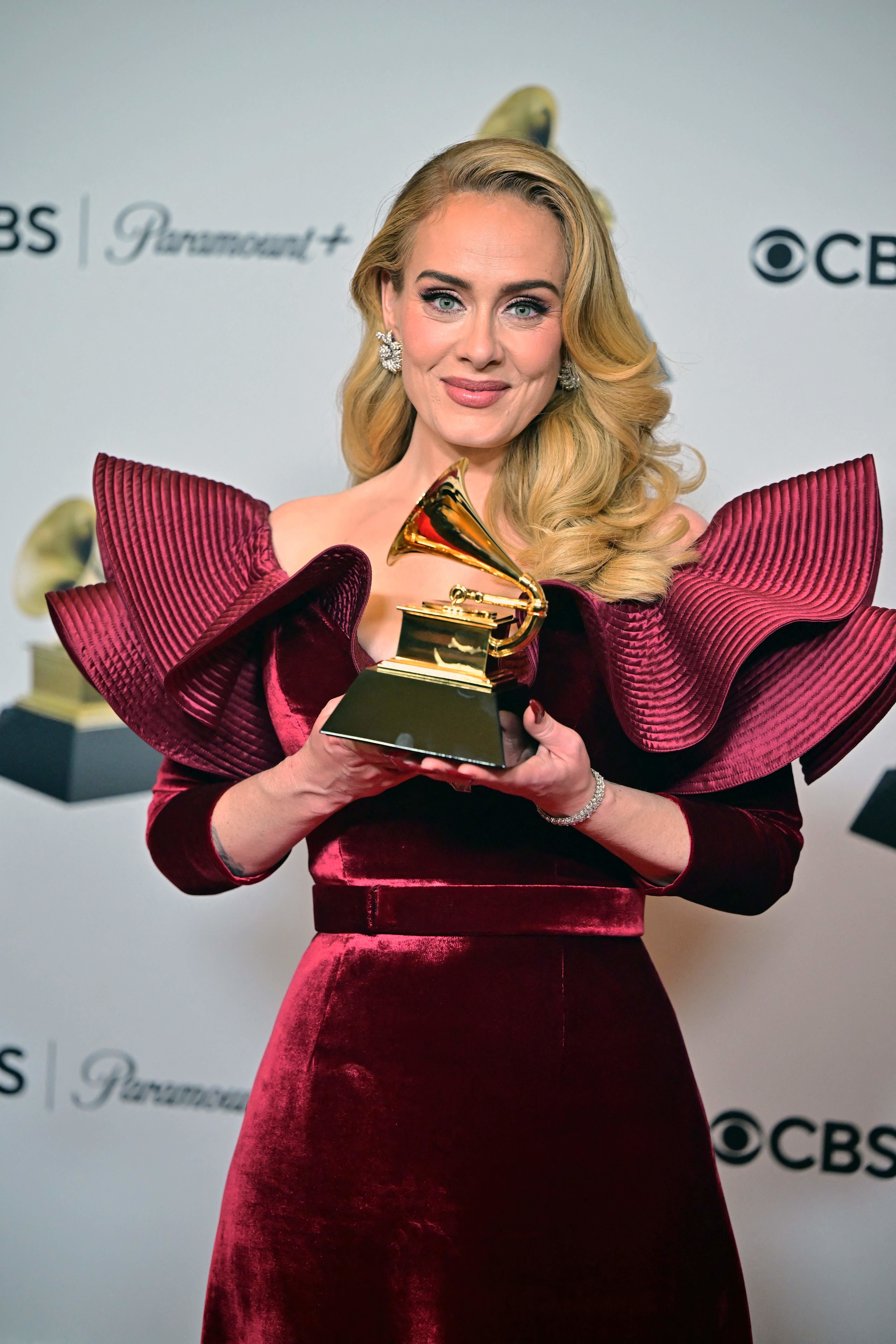 Adele holds a Grammy award while wearing an elegant dress with dramatic ruffled shoulders at a CBS and Paramount+ event