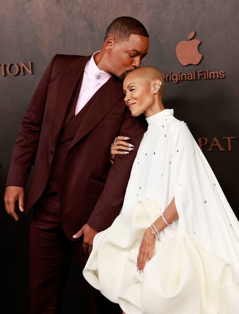 Will Smith kisses the head of Jada Pinkett Smith, who is wearing a white cape gown