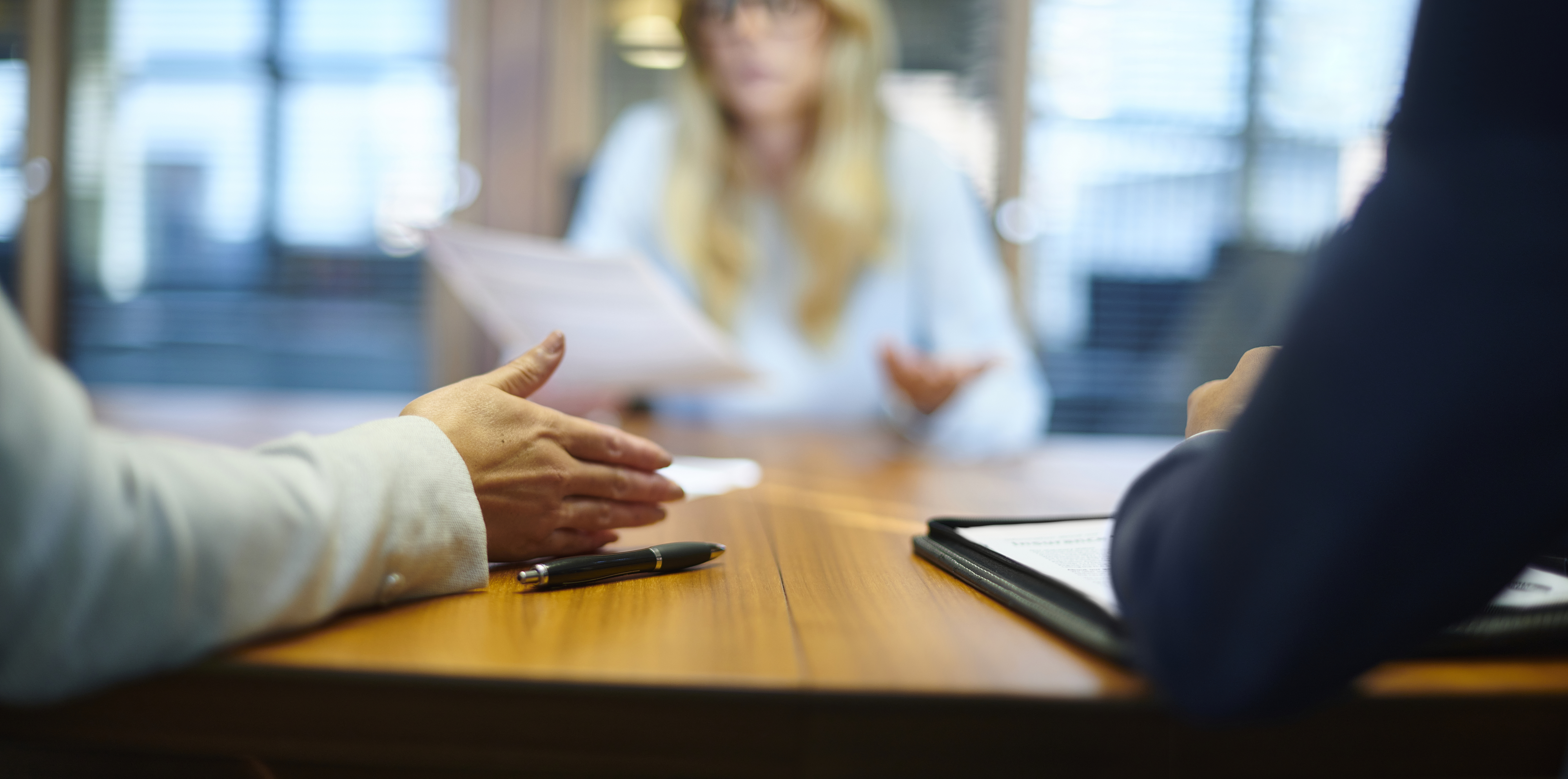 Three people are sitting around a conference table, engaged in a discussion. Out-of-focus blurry background denotes an office setting