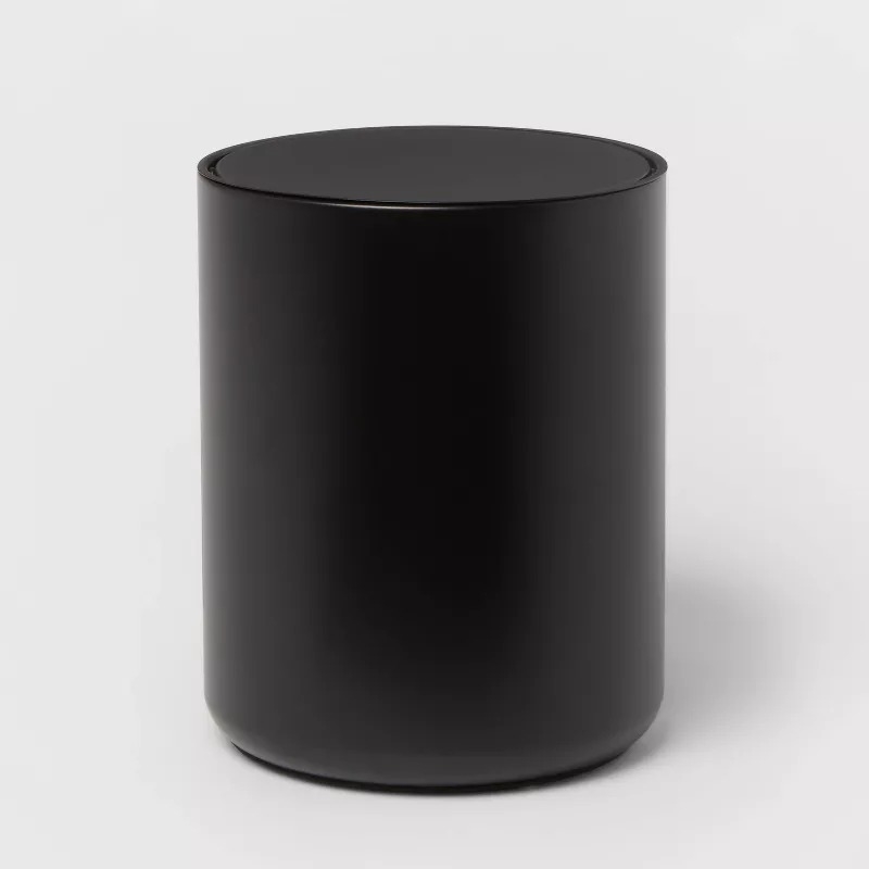A sleek, cylindrical black trash can with a smooth, minimalist design is displayed against a white background