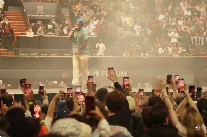 Crowd at a concert filming the performance on their phones while artists perform on stage