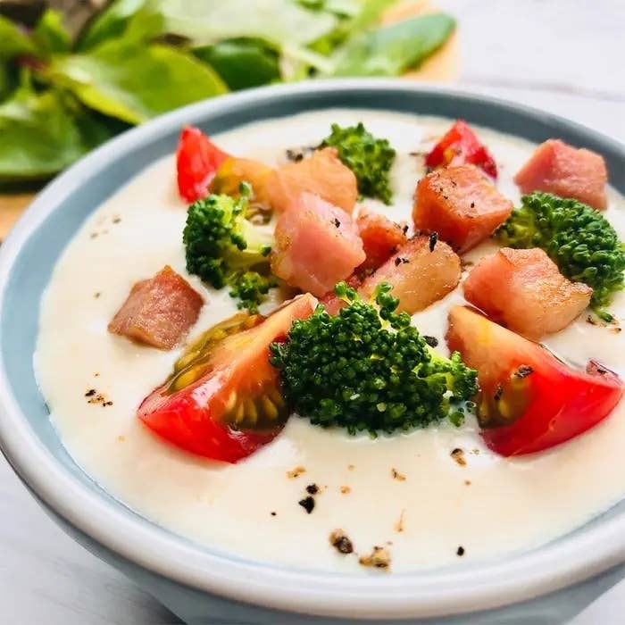 クリーミーなスープの中に、ブロッコリー、トマト、ベーコンの具が入った料理。後ろに葉野菜が見える。