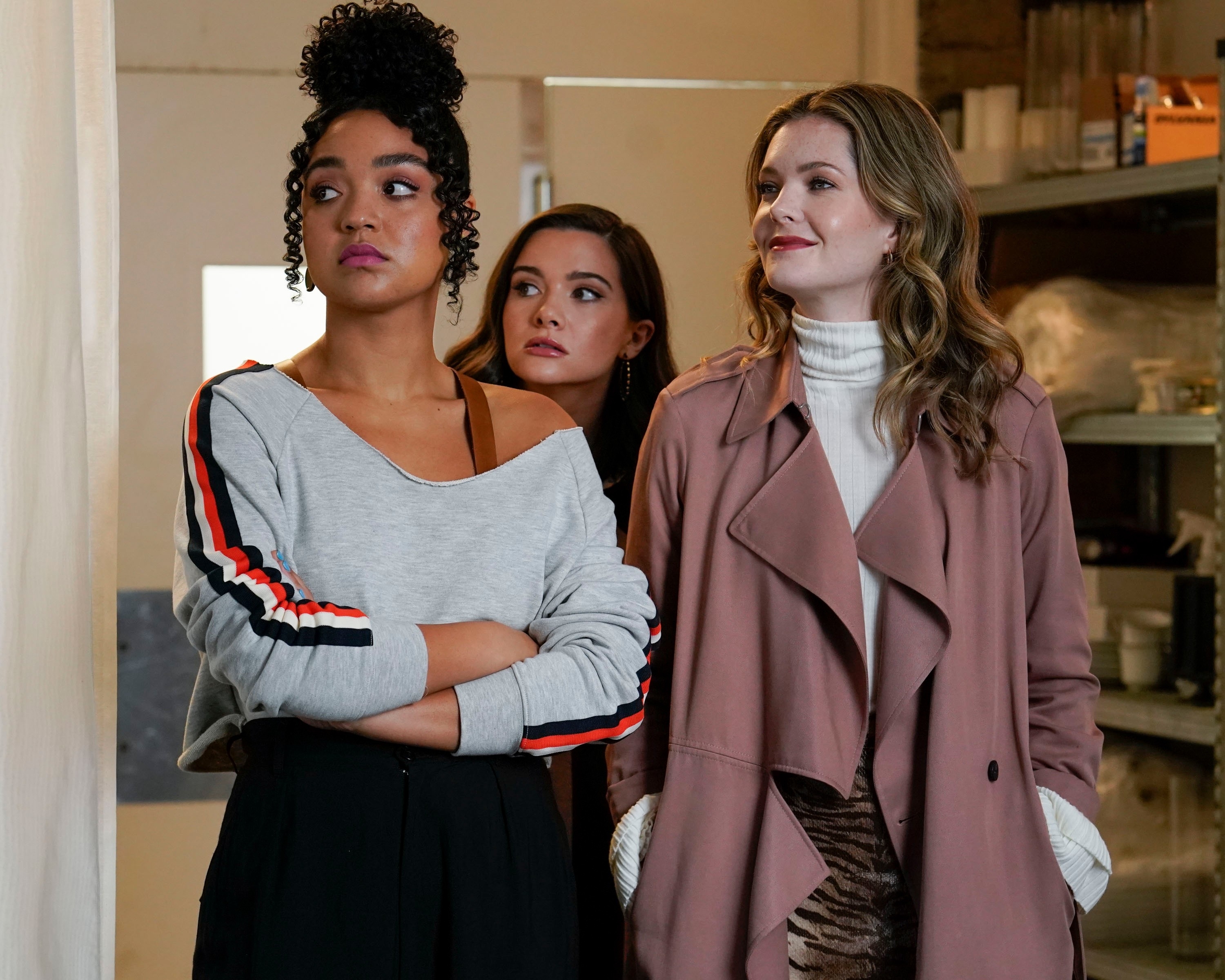 Aisha Dee, Katie Stevens, and Meghann Fahy, from "The Bold Type," stand together in casual and stylish attire, looking to the side