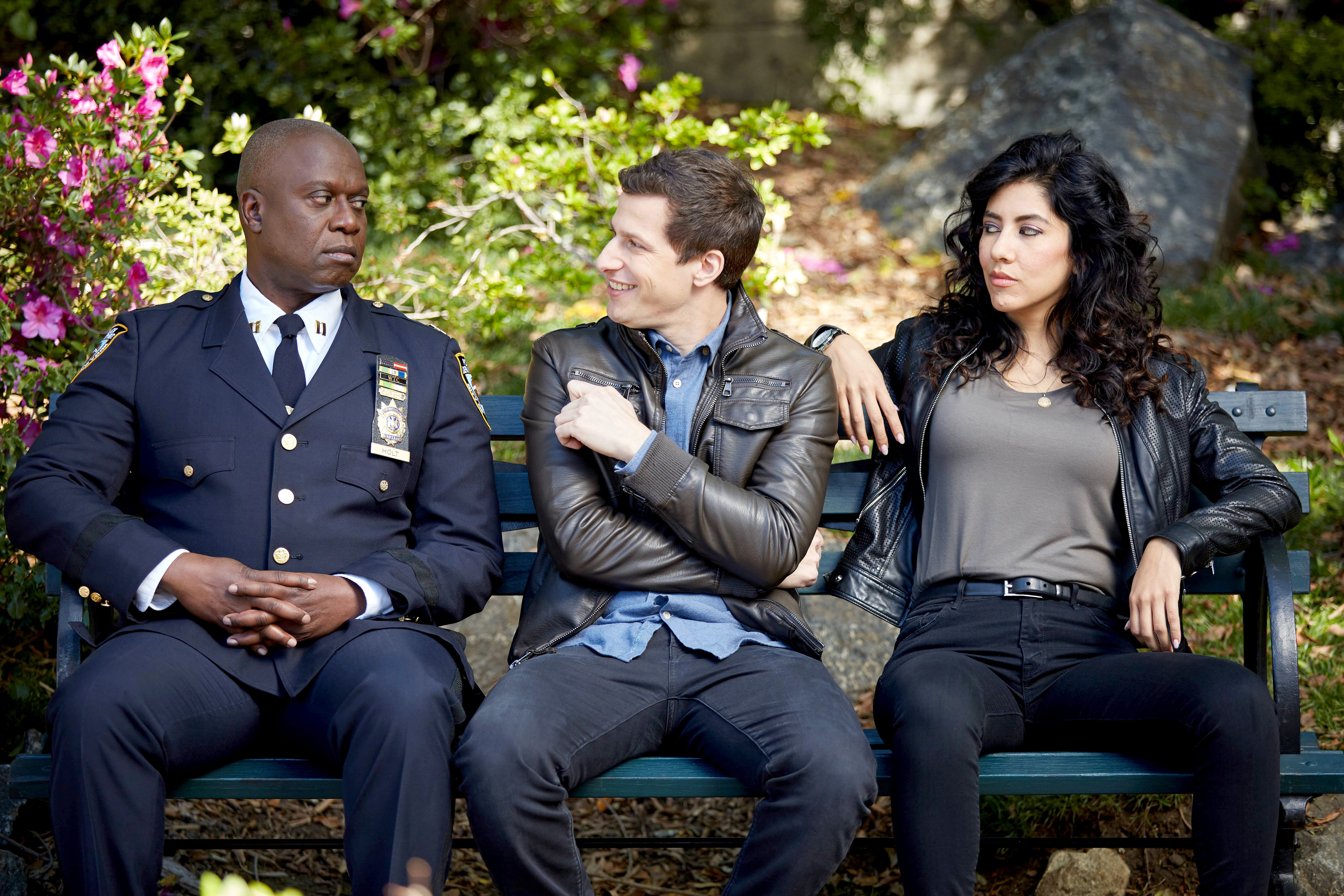 Andre Braugher, Andy Samberg, and Stephanie Beatriz sit on a park bench, with Andy smiling and engaging with Andre and Stephanie, who both appear indifferent