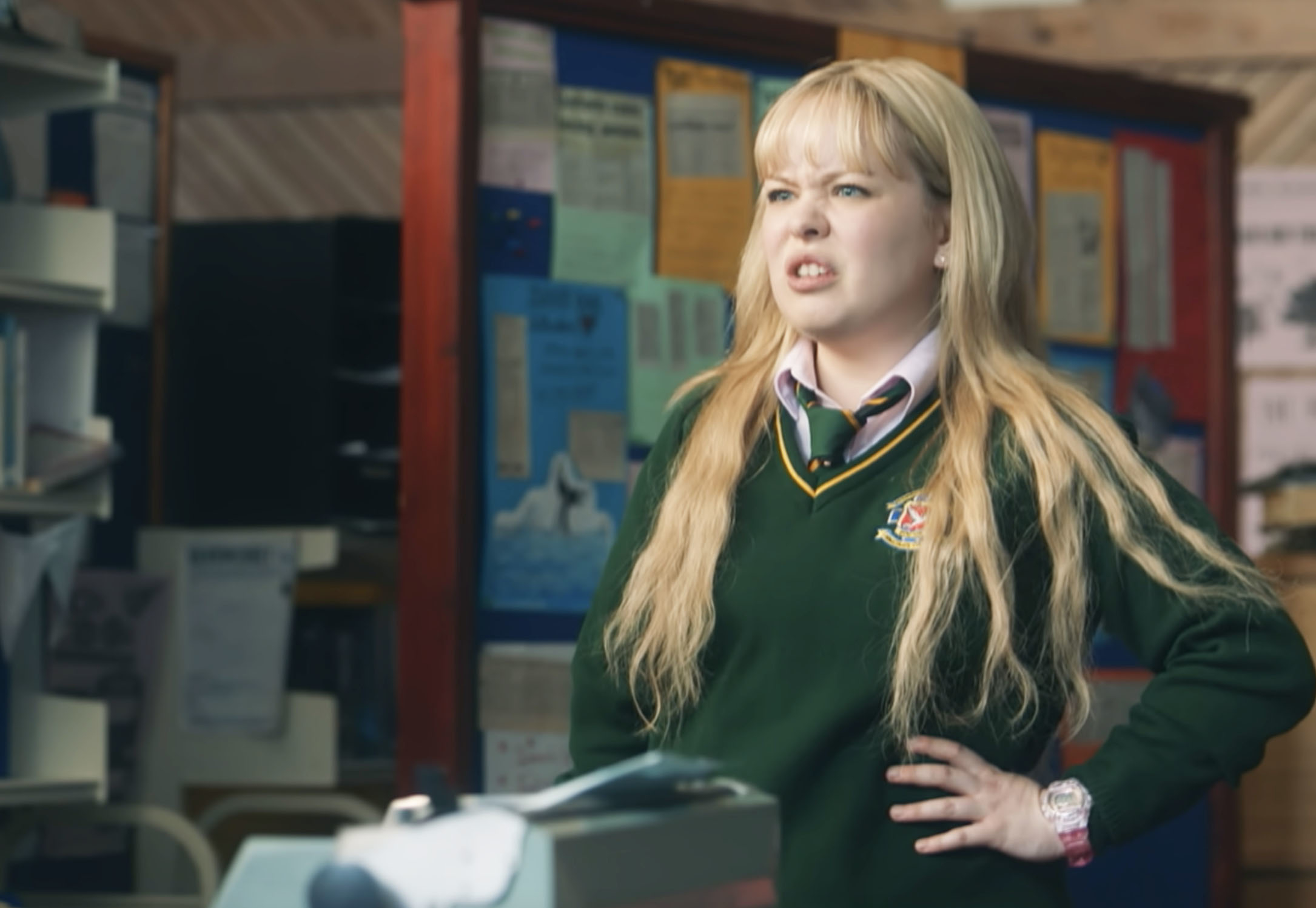 Nicola Coughlan as Clare stands in a classroom wearing a school uniform and expressing frustration, from the TV show "Derry Girls."