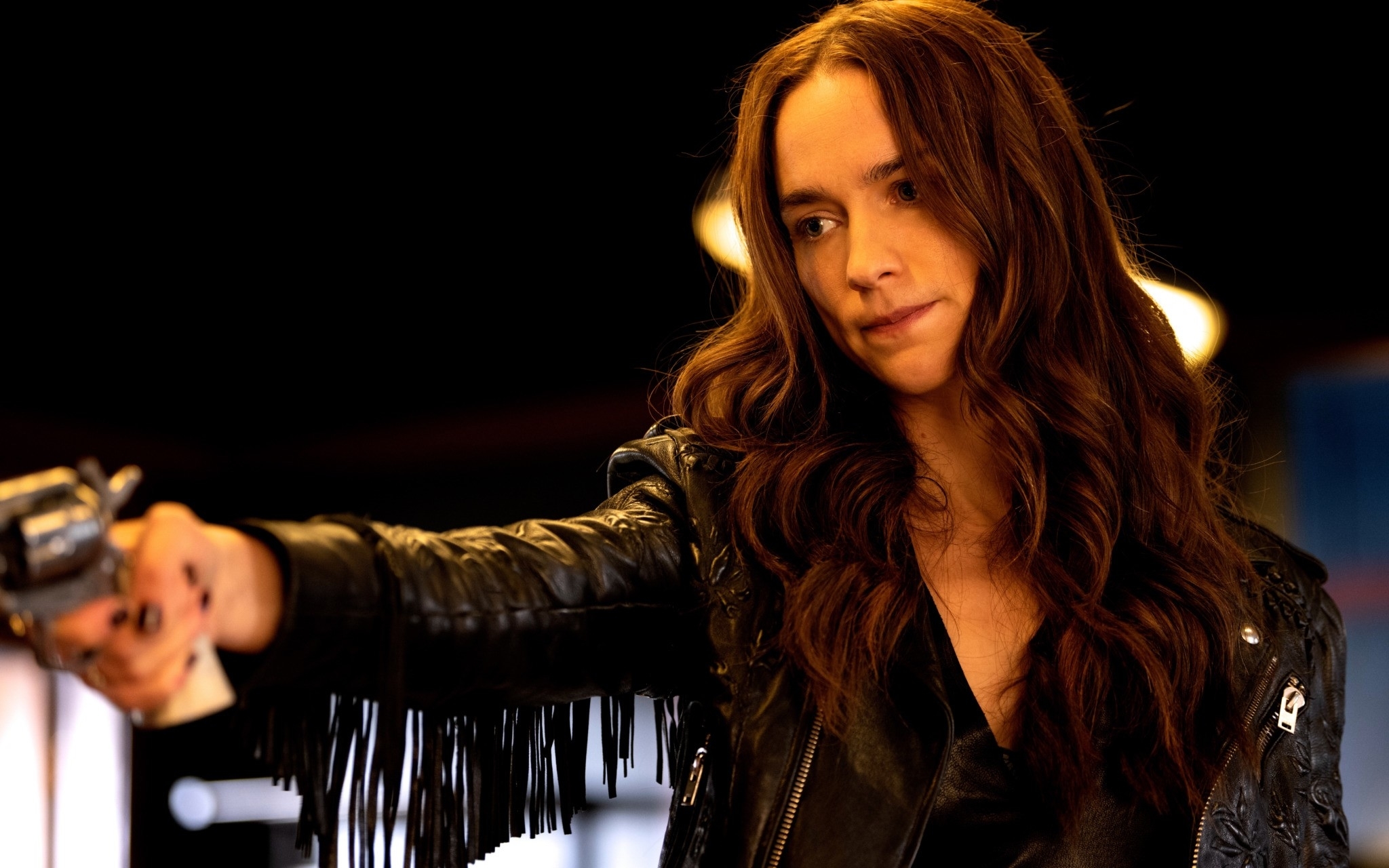 Melanie Scrofano as Wynonna Earp points a gun while wearing a leather jacket with fringe