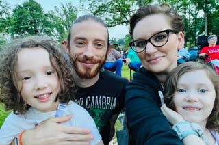 A family of four sitting outdoors. An adult man and woman, likely the parents, are with two young children. They are all smiling and appear to be enjoying their time together