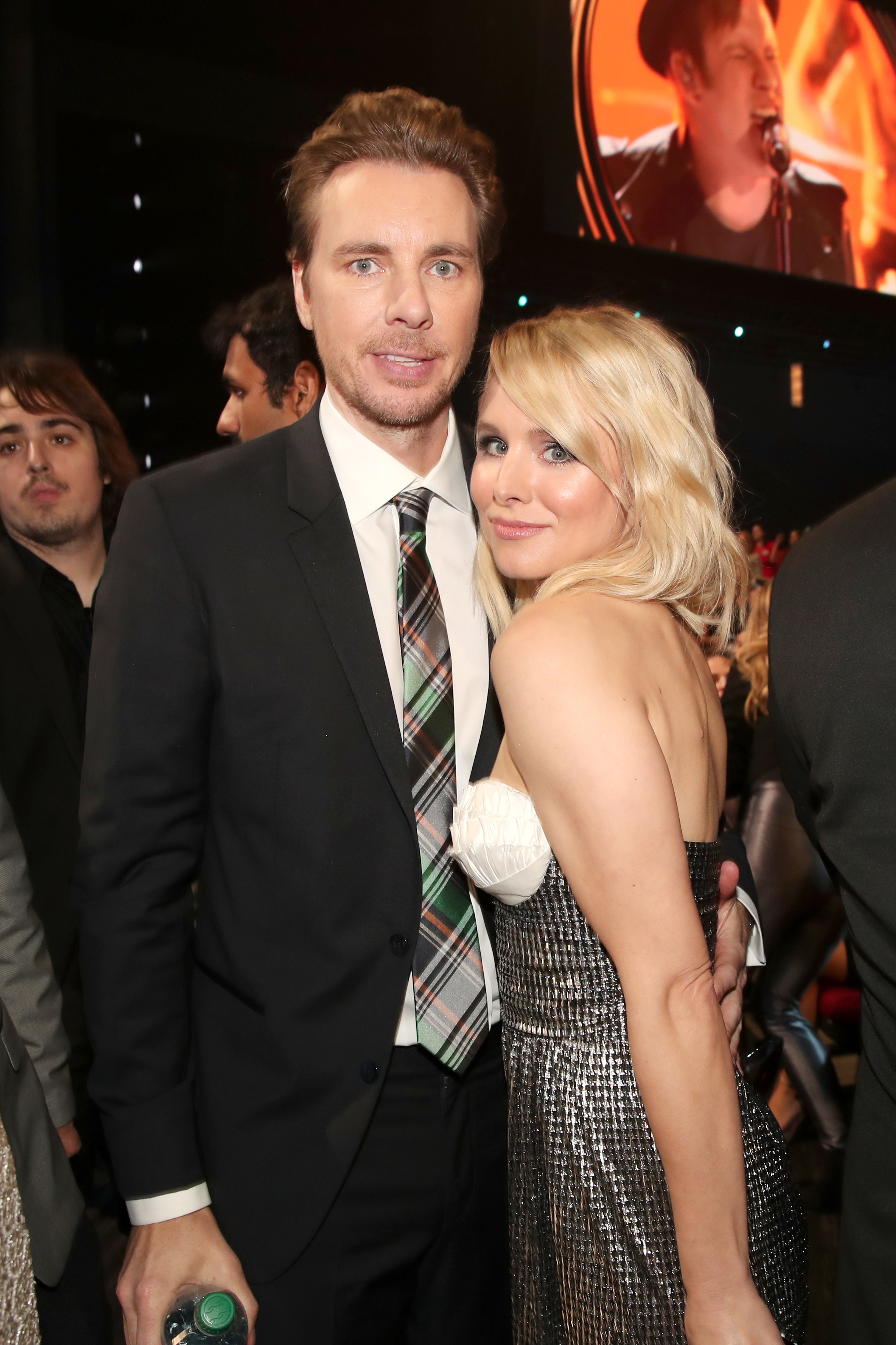 Dax Shepard in a suit with a plaid tie and Kristen Bell in a strapless, metallic gown pose together at an event