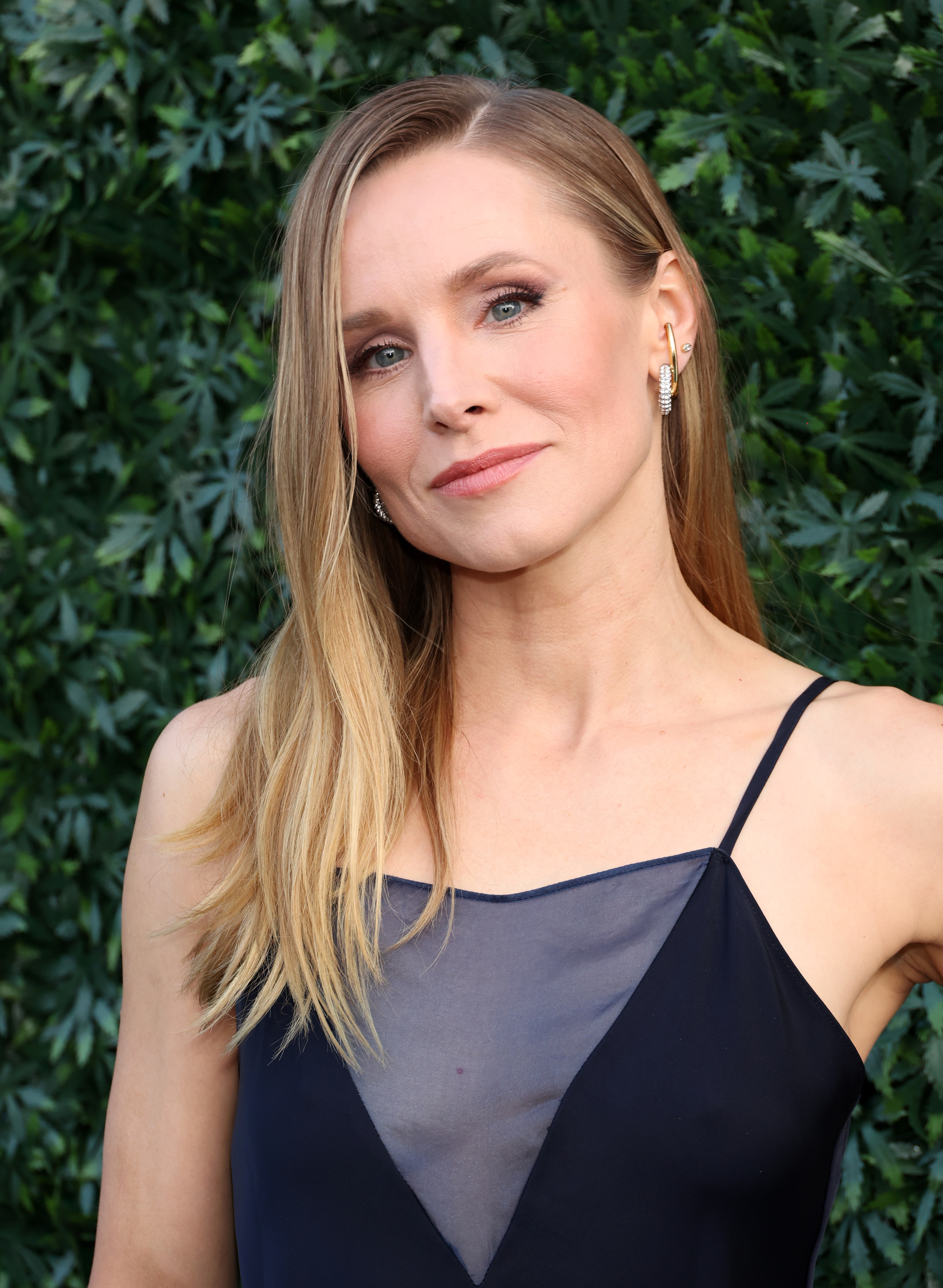 Kristen Bell poses in a sleeveless sheer-paneled dress against a foliage backdrop