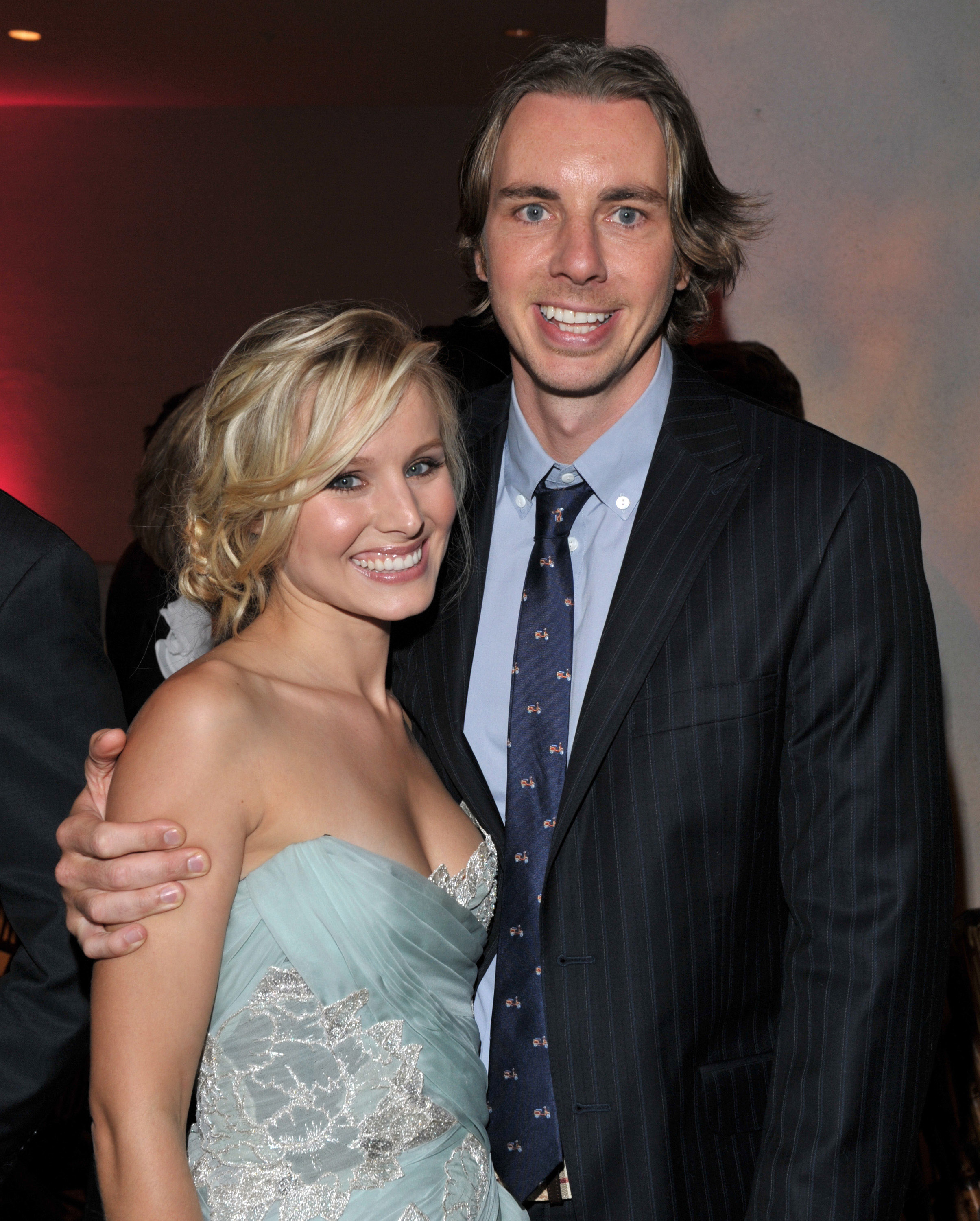 Kristen Bell and Dax Shepard are dressed elegantly at a formal event. Kristen wears a strapless dress, and Dax is in a suit with a tie, smiling at the camera