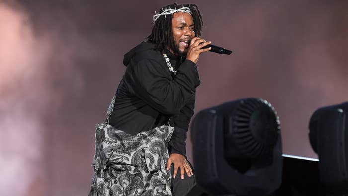 Kendrick Lamar performing on stage, wearing a crown of thorns, a black hoodie, and a patterned scarf