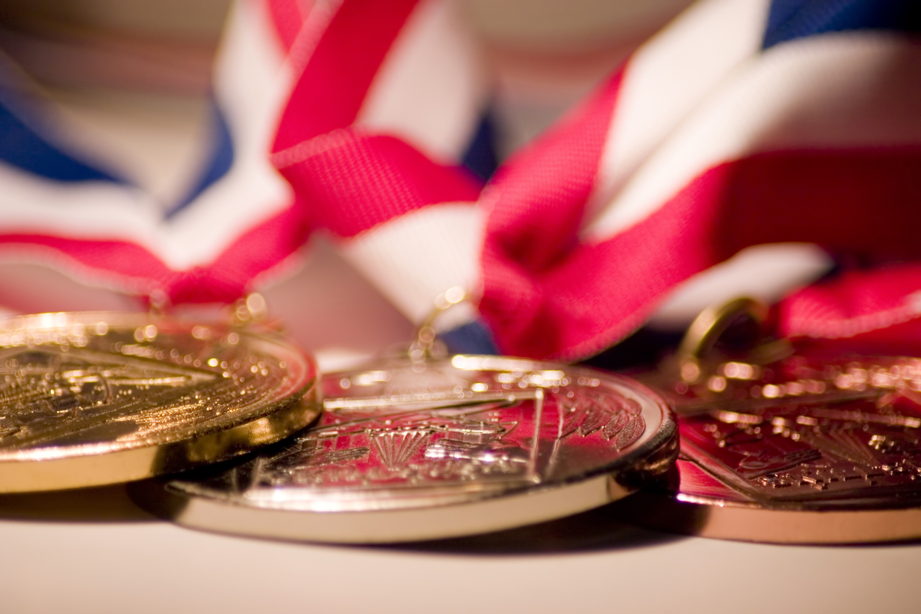 Three medals (gold, silver, and bronze) with ribbons are laid out in a close-up shot