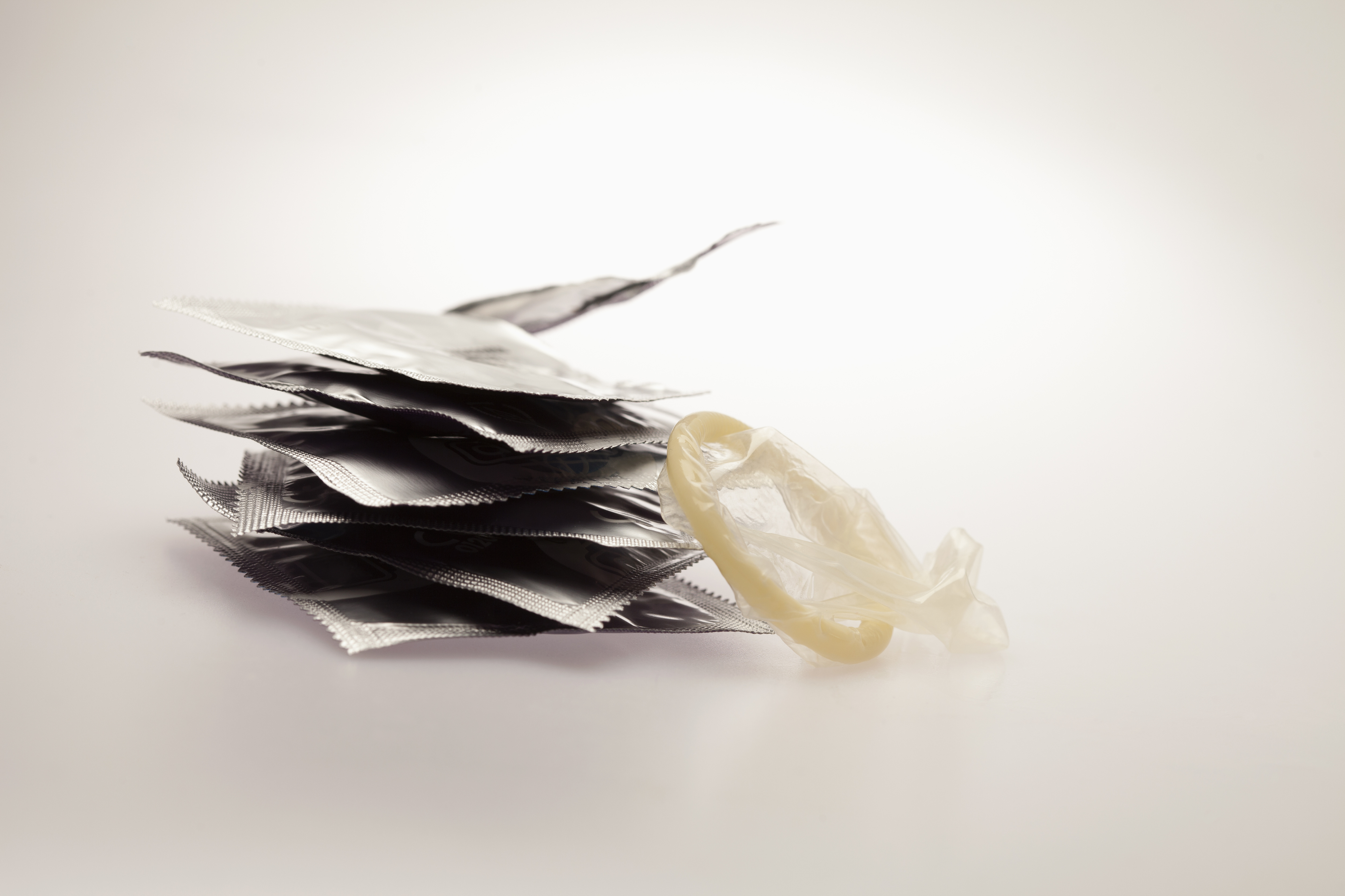 Multiple sealed condoms are stacked next to one unrolled condom