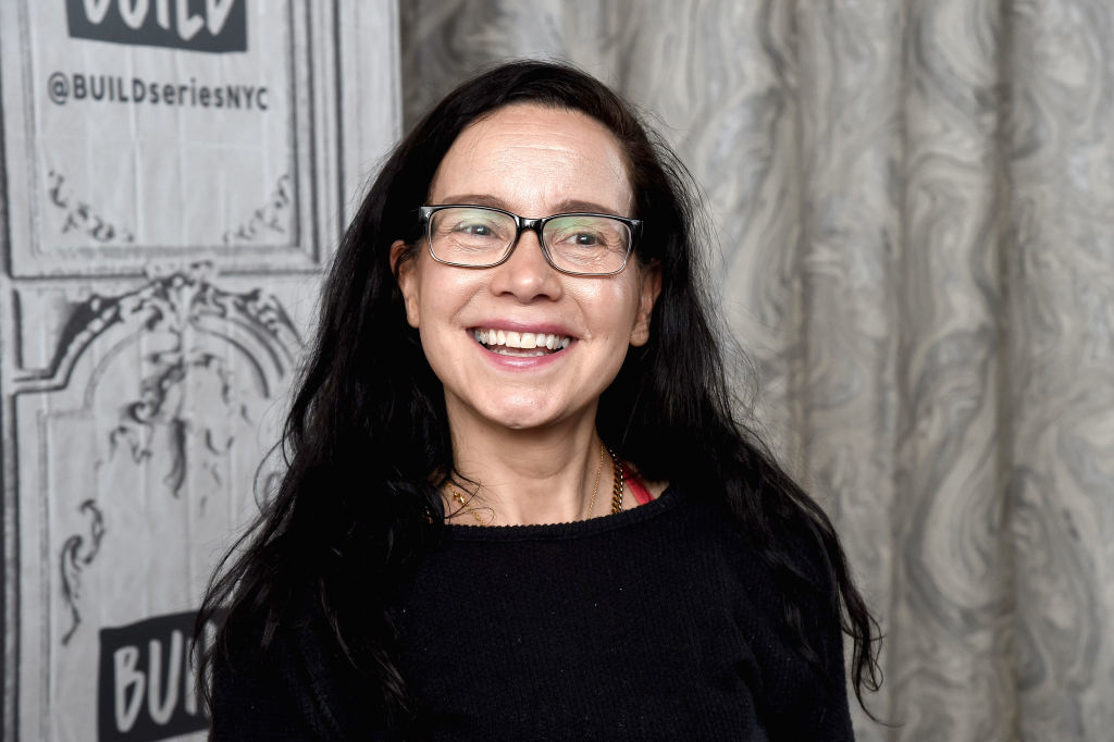 Janeane Garofalo smiles while wearing glasses and a dark top at a BUILD Series NYC event