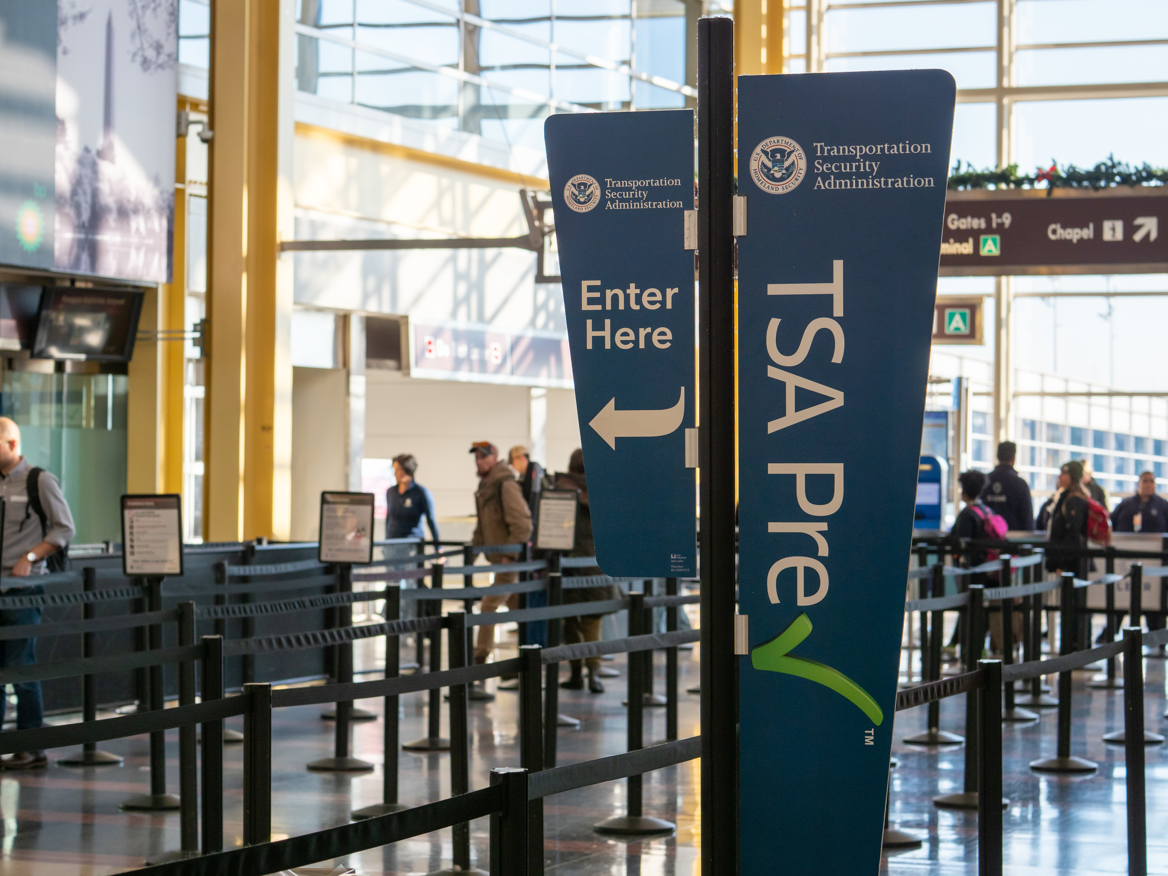 Sign for TSA PreCheck line at an airport. Travelers are in the background, going through security