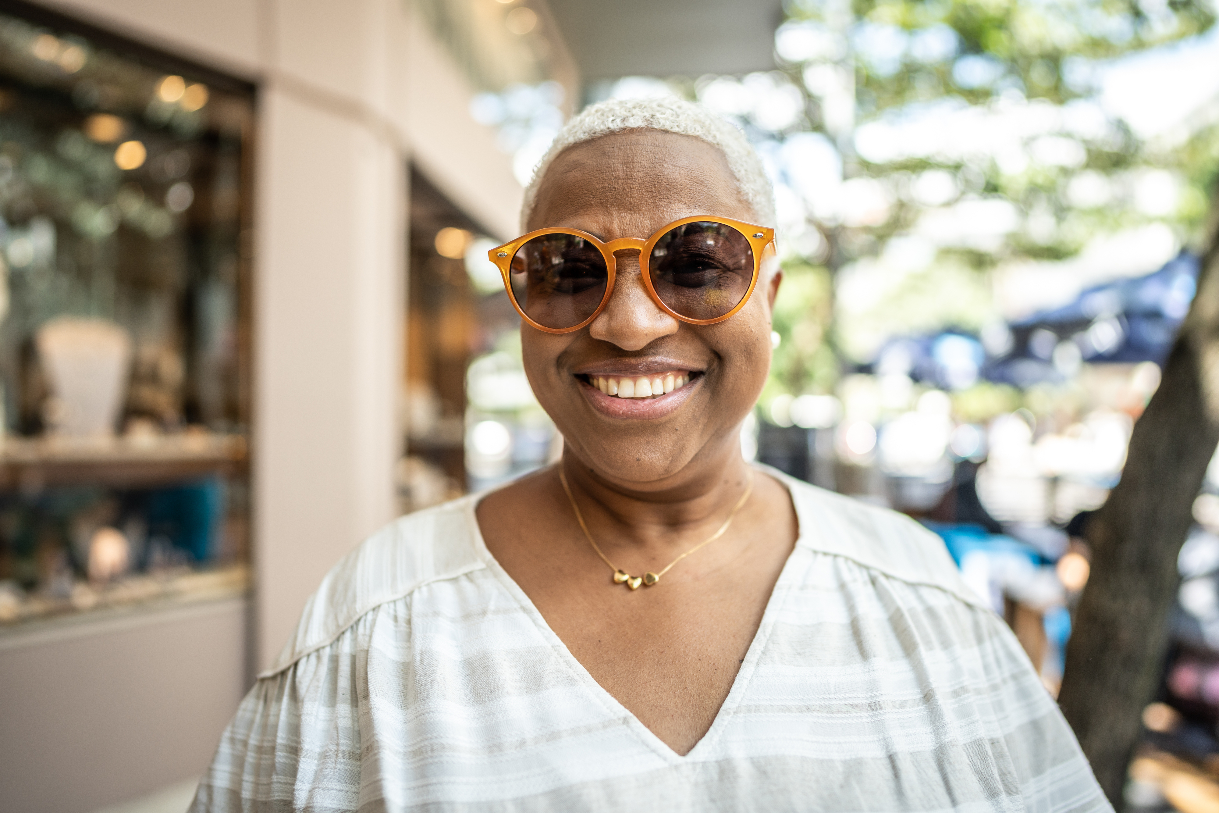 Smiling individual wearing sunglasses and a striped top, standing outdoors in a business district