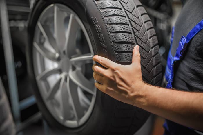 Person holding a car tire, which is mounted on a rim, in a workshop setting. No text present