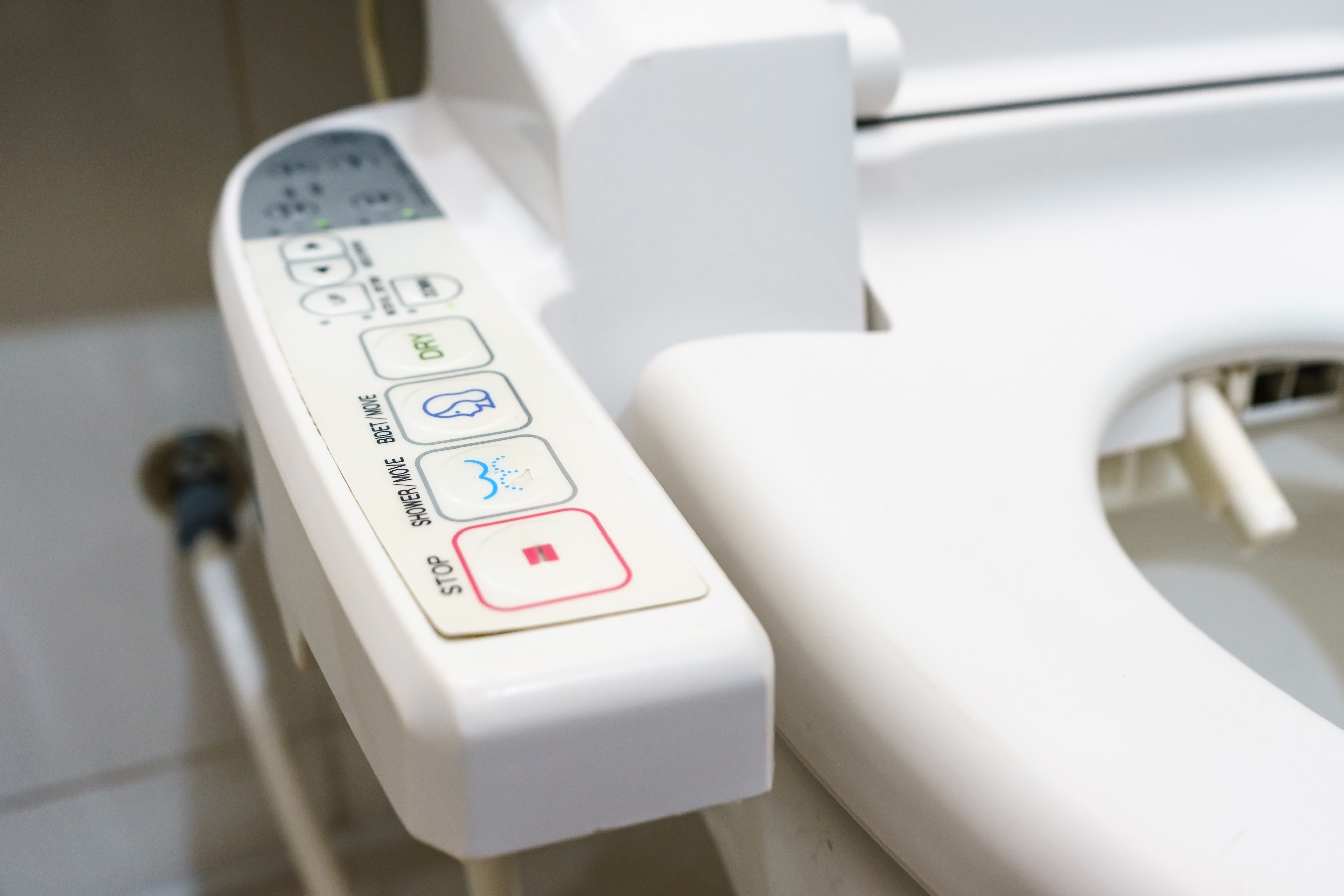 Close-up of a high-tech toilet control panel with buttons for various functions, including stop, spray, and bidet