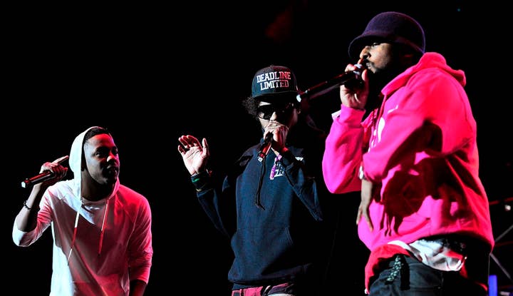 Kendrick Lamar, Ab-Soul, and Schoolboy Q performing on stage, holding microphones and engaging with the audience