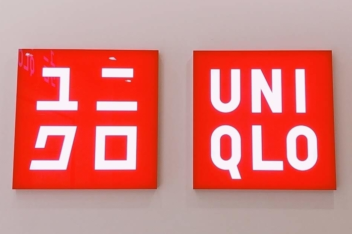 Two red signs with white text. Left sign shows Japanese characters. Right sign shows &ldquo;UNIQLO.&quot;