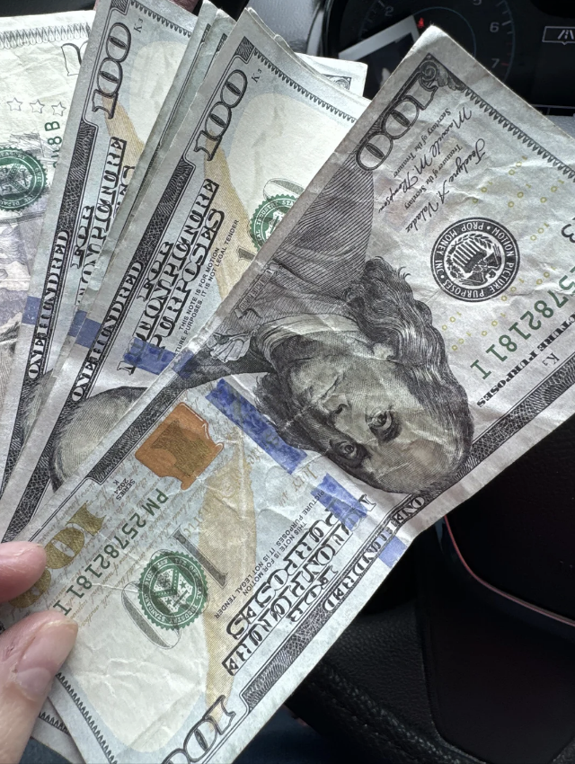 A hand holding several US $100 bills, with visible images of Benjamin Franklin on the notes