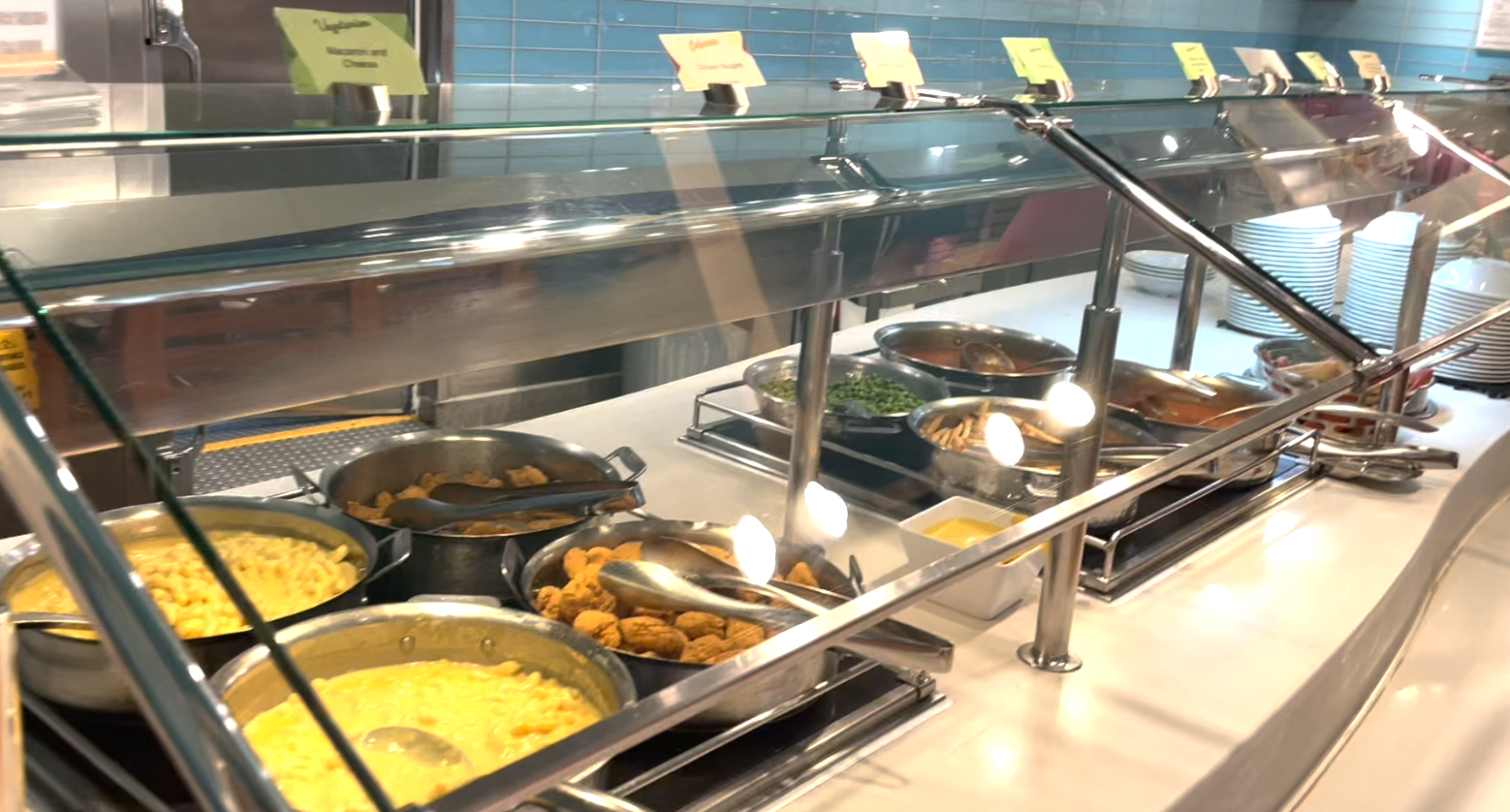 Buffet setup featuring various dishes including scrambled eggs, mac and cheese, fried chicken, and green beans. Plates and utensils are placed at the end