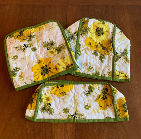 Three kitchen cloths with yellow flower designs and green borders are arranged on a wooden table