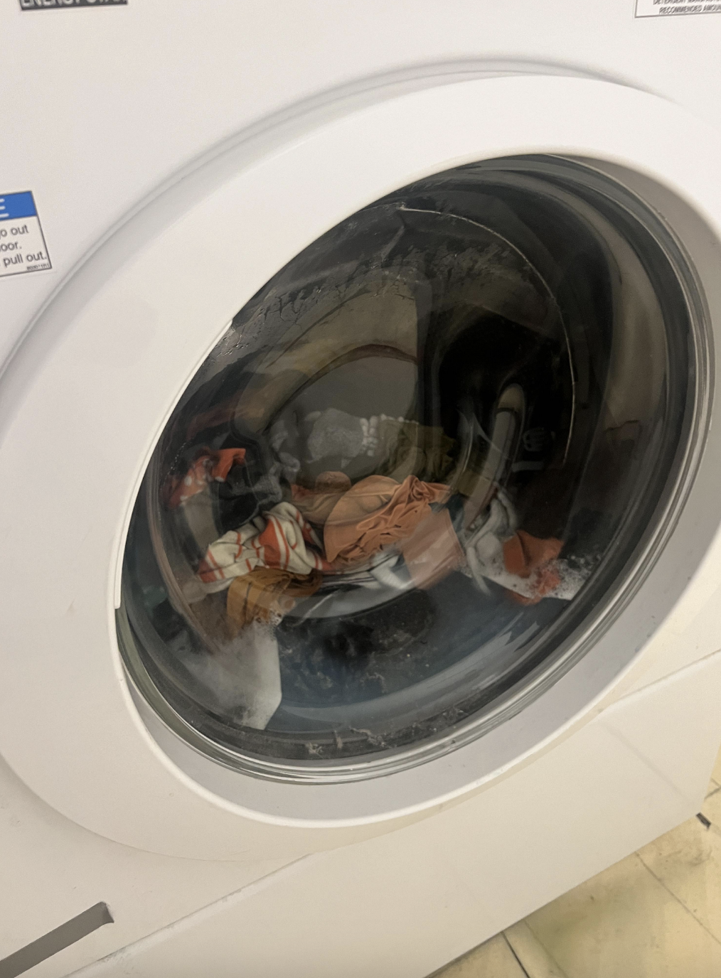 A washing machine with clothes visible through the front glass door during a wash cycle