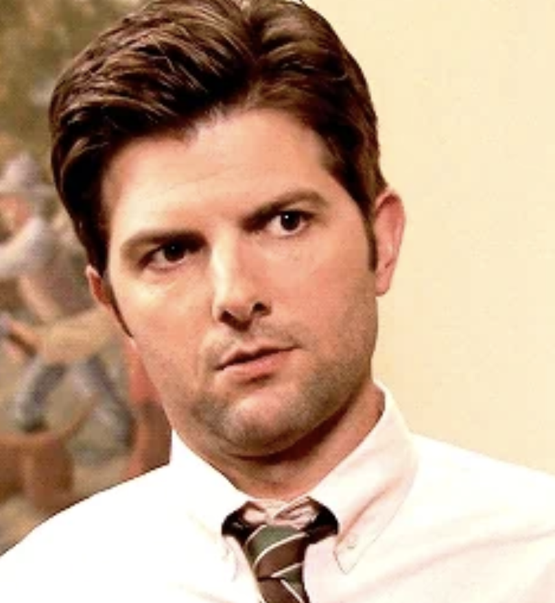 Adam Scott wearing a white dress shirt and a striped tie, appears to be indoors with a neutral expression