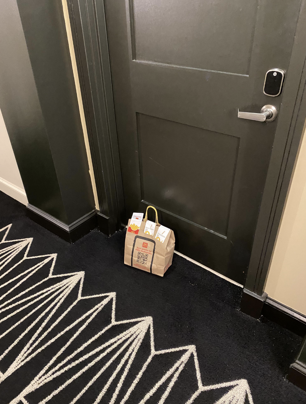 Food delivery bag placed outside a closed door in a hallway with patterned carpet