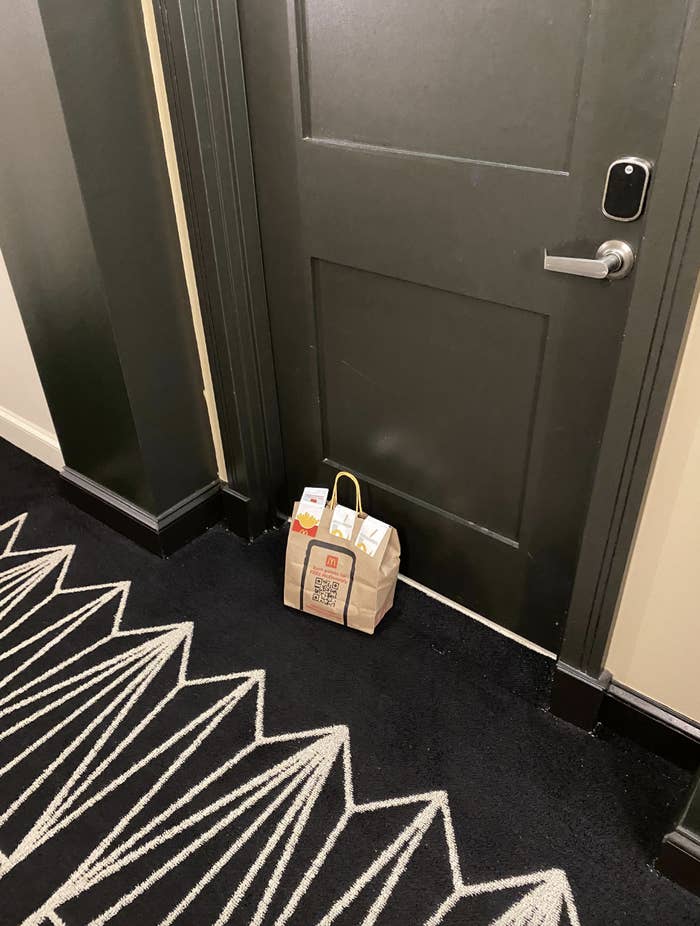 Food delivery bag placed outside a closed door in a hallway with patterned carpet