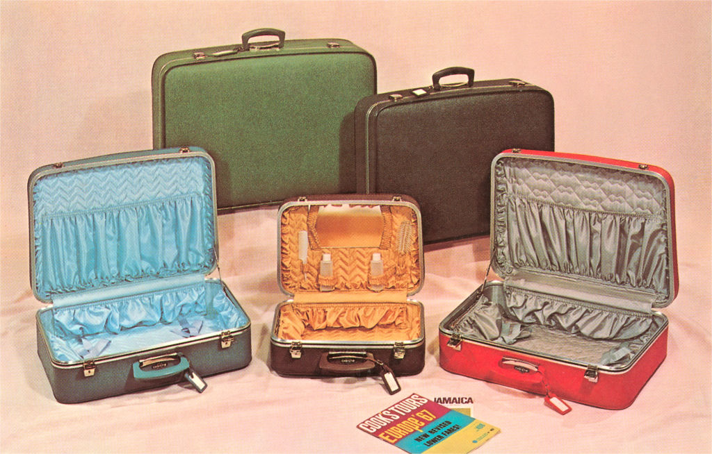 Three open and two closed vintage suitcases. The open suitcases reveal patterned linings. A paper labeled "Travel Tips Jamaica" is in front
