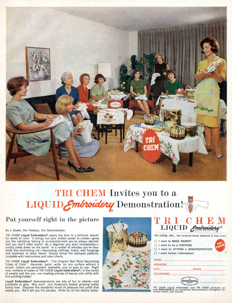 A group of women gather in a living room for a Tri Chem Liquid Embroidery demonstration. A hostess shows various embroidery products and techniques on tables
