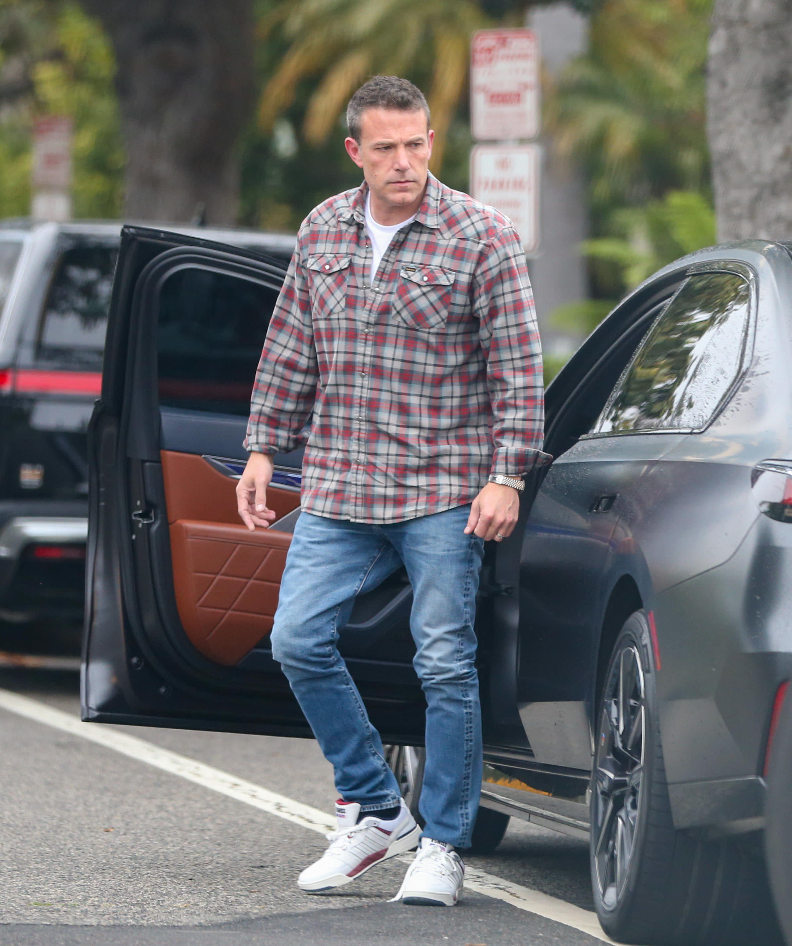 Ben Affleck steps out of a car wearing a plaid shirt, jeans, and sneakers