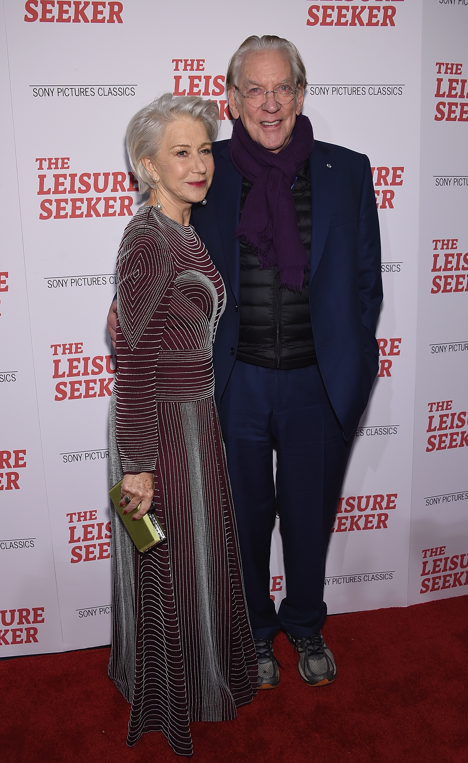 Helen Mirren and Donald Sutherland pose together on the red carpet at "The Leisure Seeker" premiere. Mirren wears a long-sleeve striped dress, Sutherland wears a suit